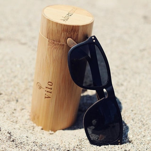 Personalised sunglasses engraving custom made for you. Wooden sunglasses beside a bamboo case in the sand